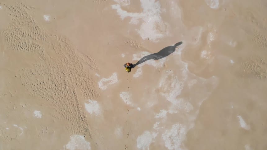 A person is walking on sand wearing a backpack in midday