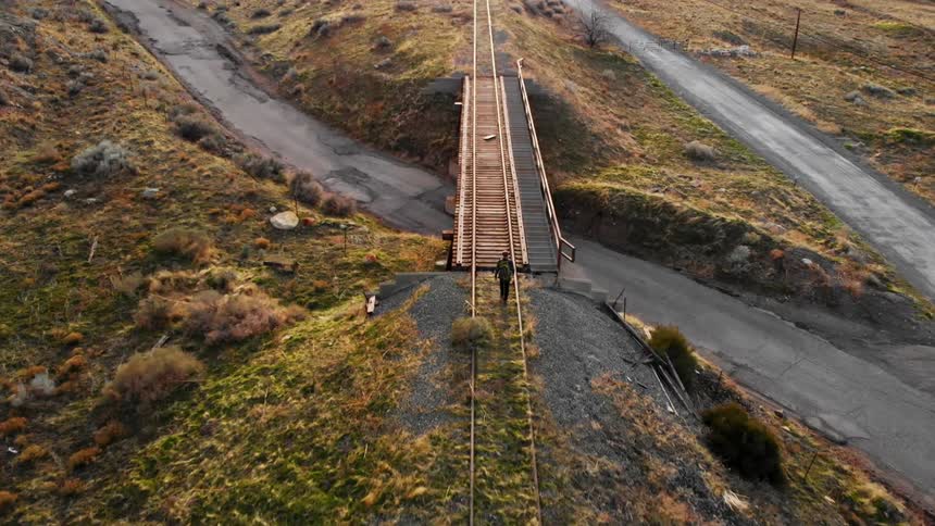 A hiker walks along a train track in the countryside during the day