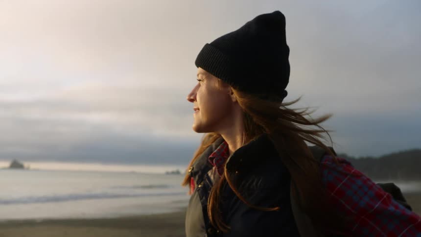 Young smiling woman walking on the sand next to the ocean at sunset
