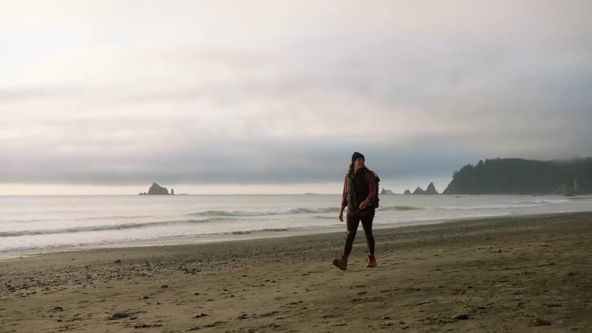 Woman walks across beach as fog covers promontory