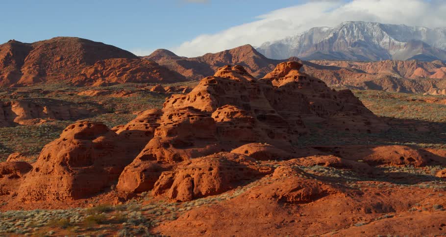 A desert with cliffs and hills with a mountain range the sky and clouds in the background