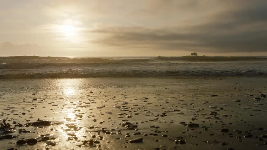 Ocean waves roll in at the beach under a golden sun