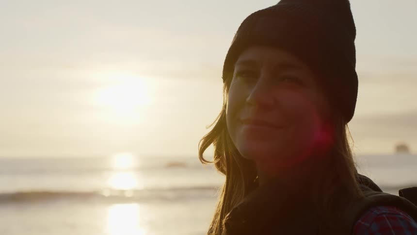 A happy woman smiling while standing on a beach on a chilly day