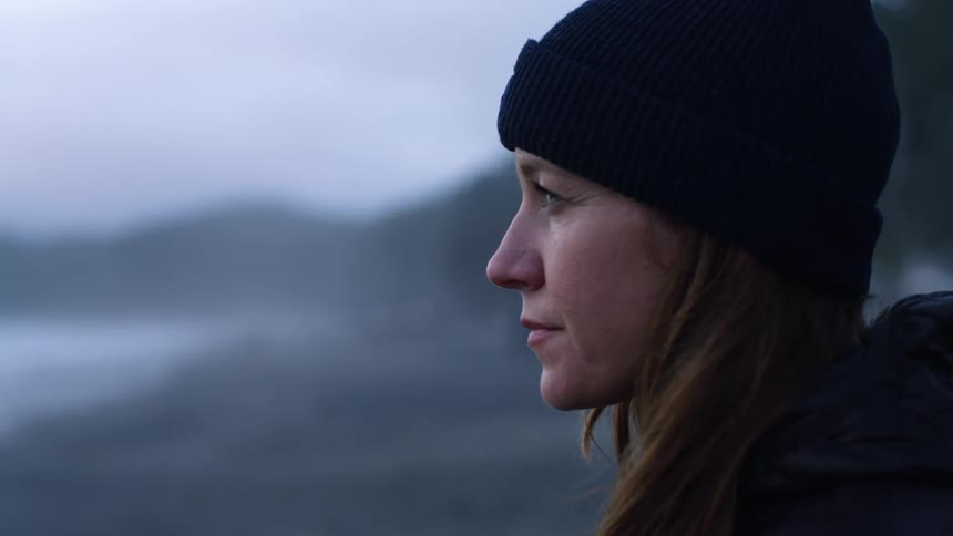 A woman wearing a beanie looks off in the distance contemplatively