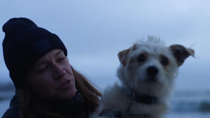 A woman holds an alert pet dog in her arms as she stands at the coast