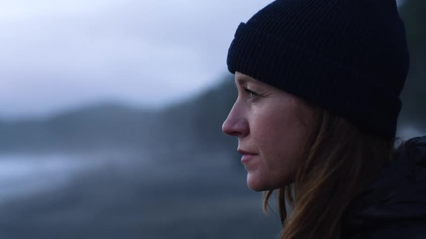 Female person wearing black knit hat is on the beach in deep thought