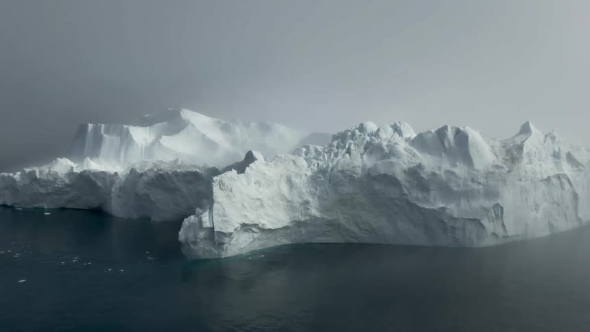 An ice glacier in a body of water with fog in the background