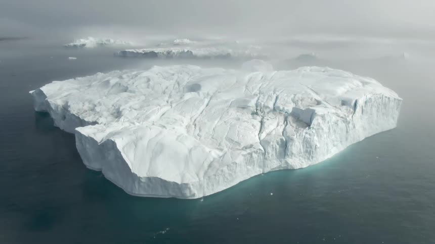 A snow covered glacier in the middle of the ocean with mist in the background