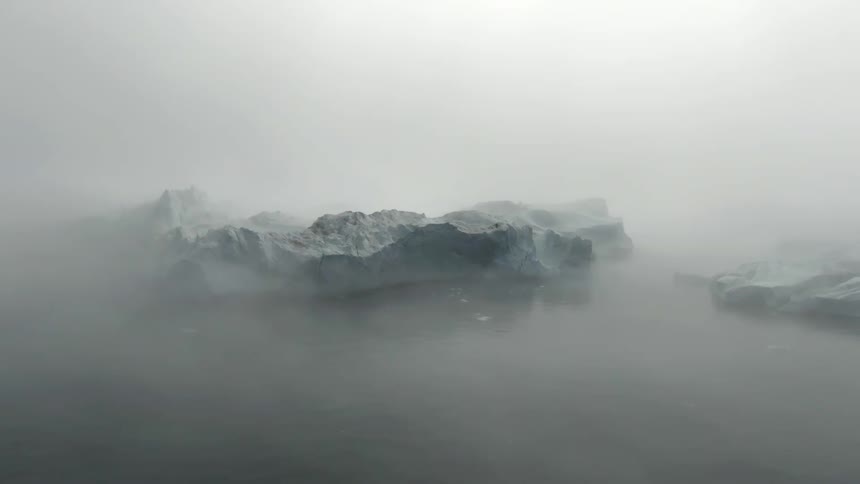 Snowy icebergs in an ocean on a foggy day