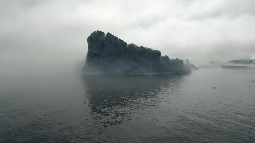 A large ice berg float atop the ocean water under a very cloudy sky