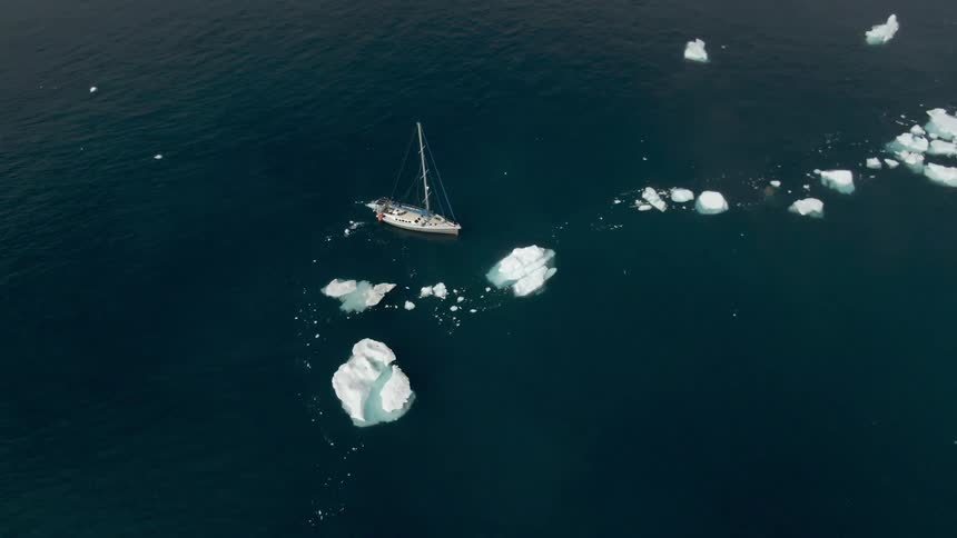 Boat sits in ocean around broken icebergs dark water lightly rippling
