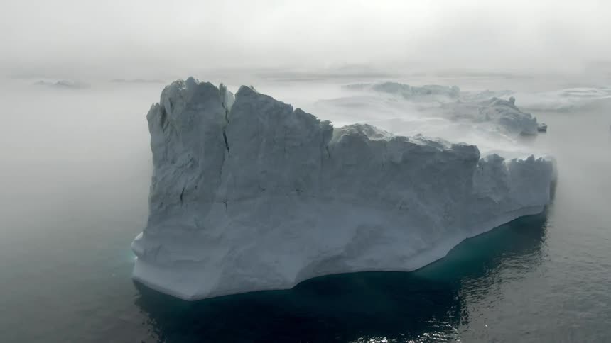 Large peaked iceberg floating in a misty arctic ocean among other icebergs