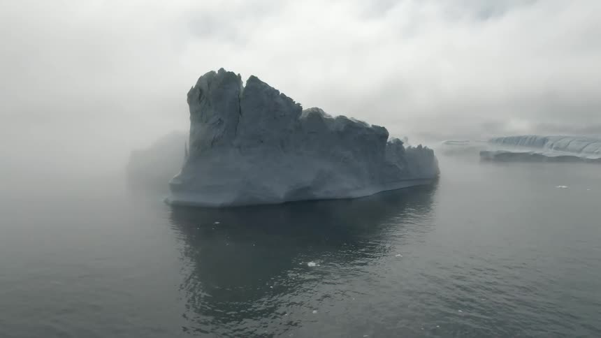 Boat sits in ocean large icebergs some tall on a cloudy foggy day