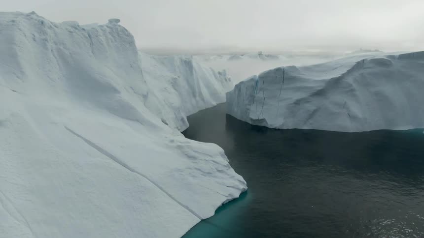 Snow covered terrain surrounded by blue green body of water with mist in the background