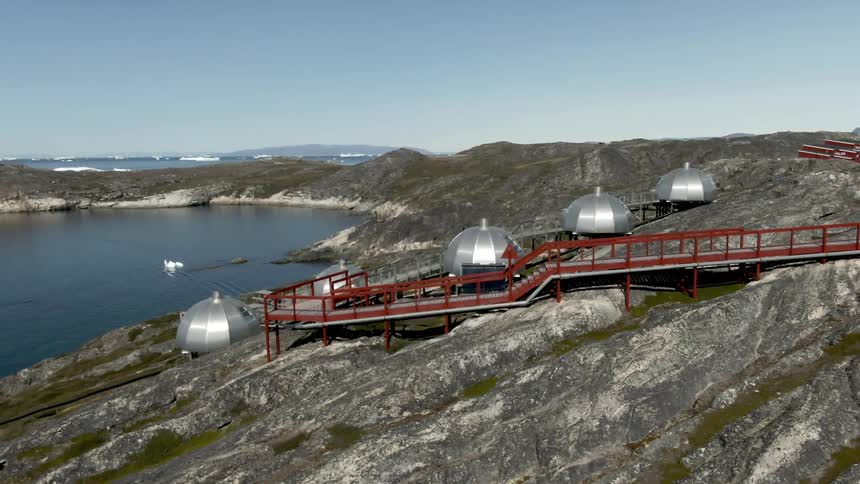 Five silver dome structures sit on the side of a hill overlooking a body of water