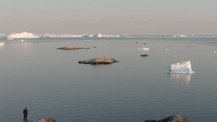 Ice floats on ocean as person walk across rocky shore