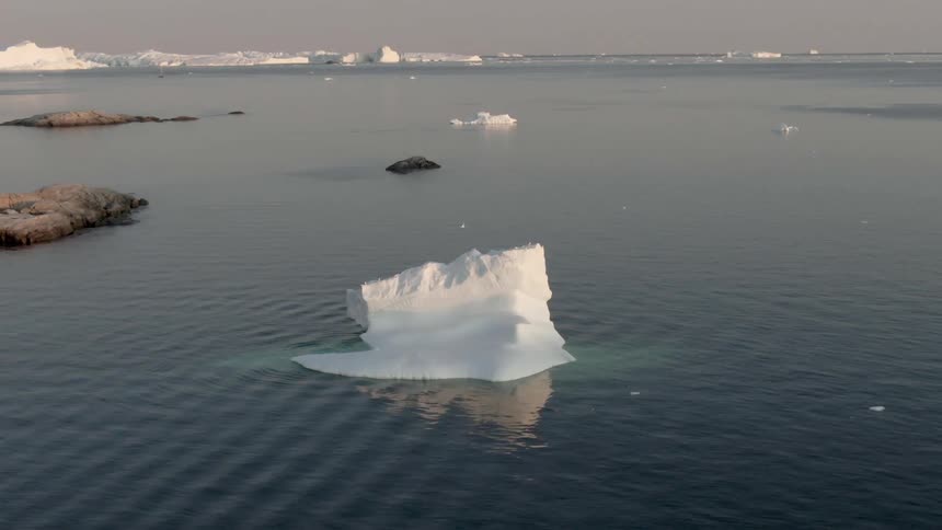 An iceberg floats across the ocean in the evening