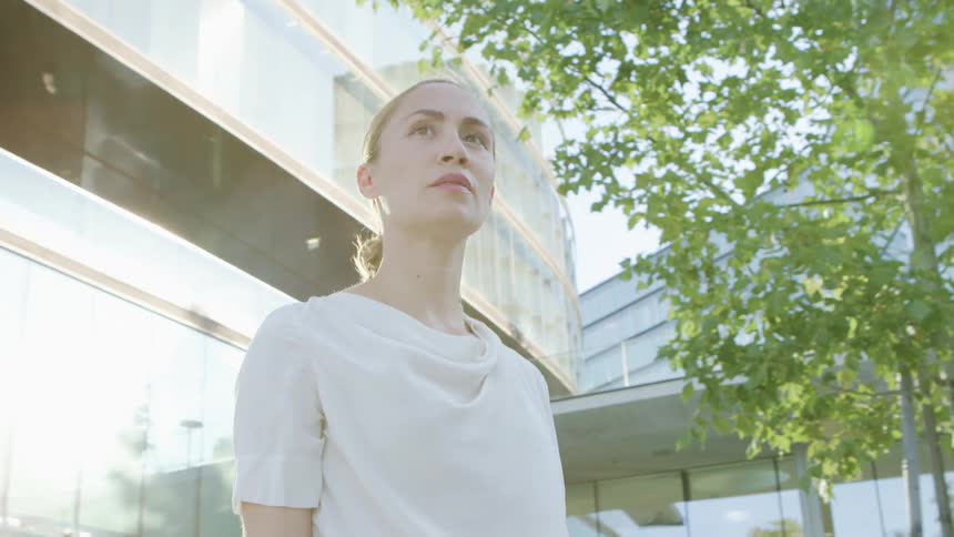Blonde businesswoman with a white blouse walks in front of office buildings