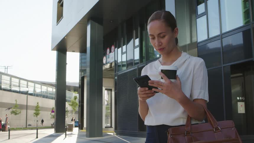A white female standing in front of an office building holding and looking at cell phone