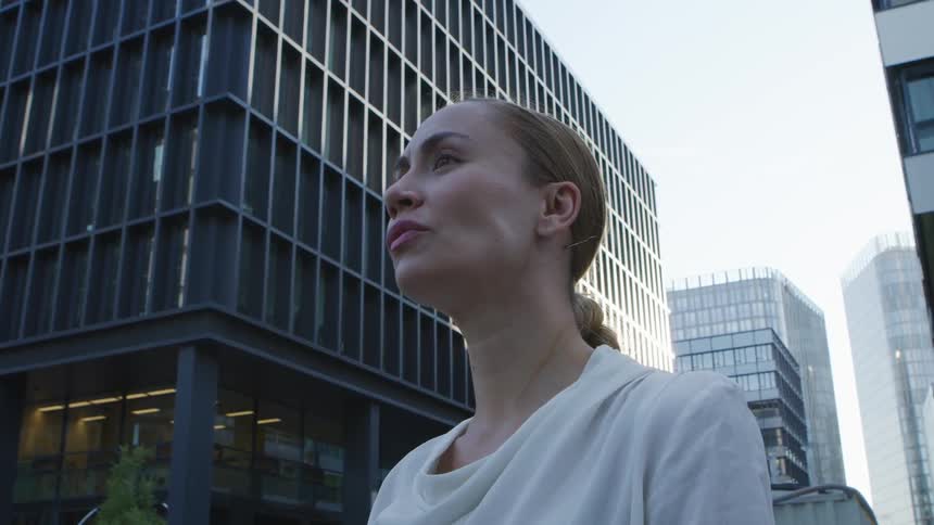Businesswoman with a white blouse looks around in front of the office buildings