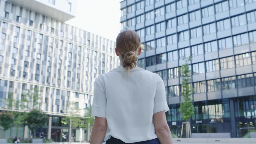 A woman walks towards an office building during the day in a city setting