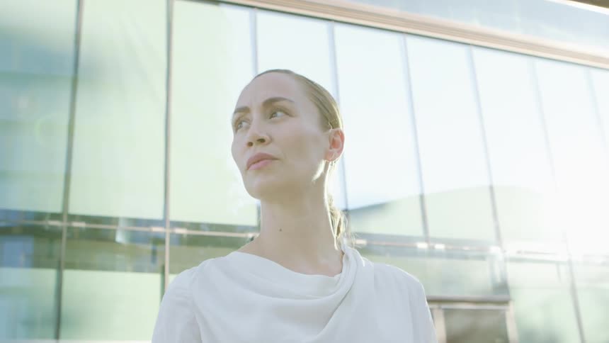 A woman gazes around at her surroundings while standing outdoors in a city on a sunny day