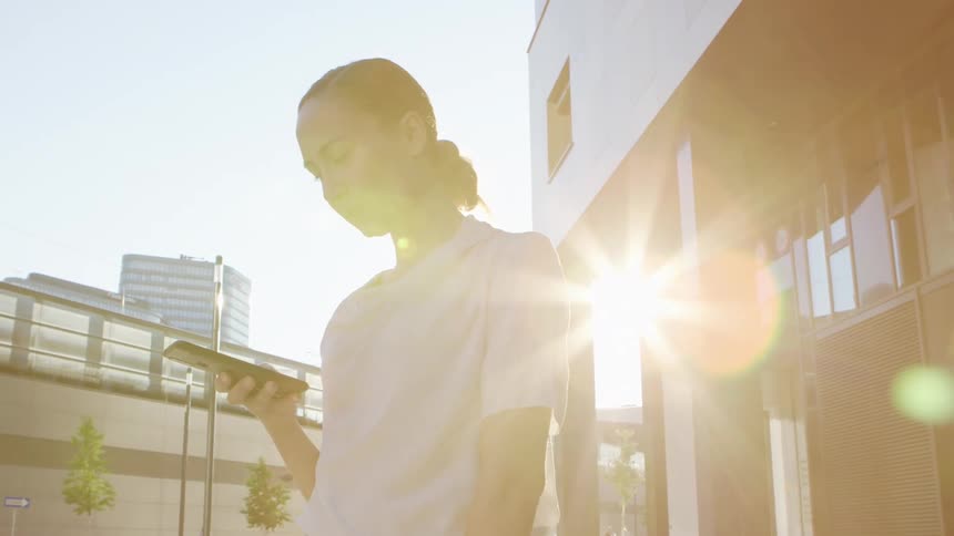 A woman uses her smart phone while standing outside her office building on a sunny day