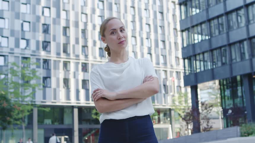 Woman in a white blouse crossing her arms with buildings in the background