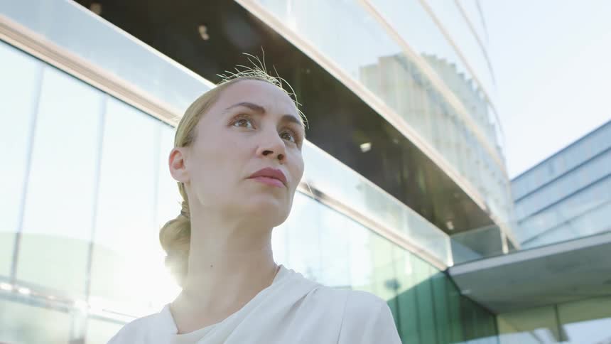 Blonde businesswoman with a white blouse looks around in front of office buildings