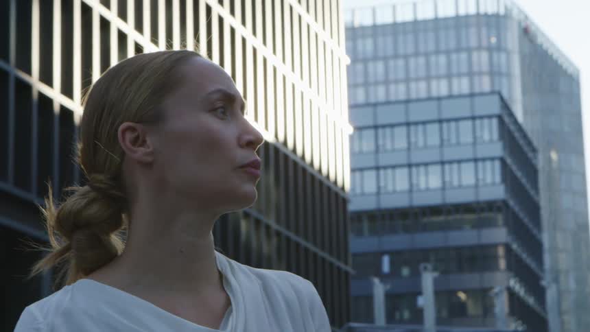 A woman looks around at her surroundings while standing outdoors in a metropolis during the day