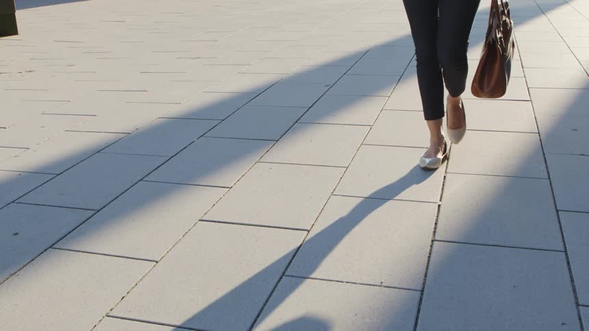 Woman walks holding a handbag on a sidewalk at daytime