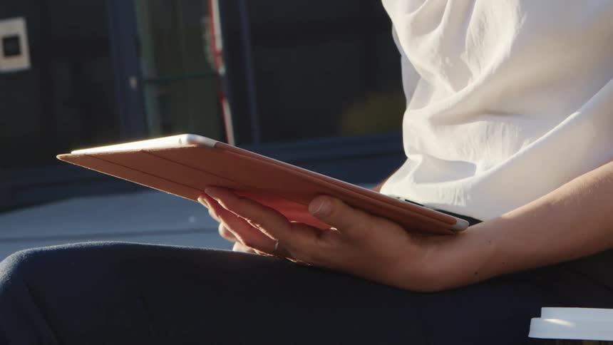 A woman sitting outside of a building uses a tablet
