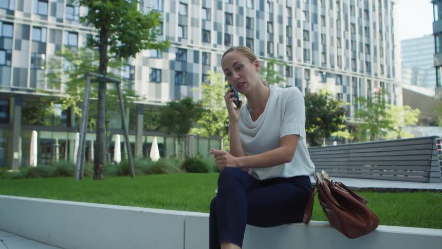 Woman sitting near some city buildings talking on the phone