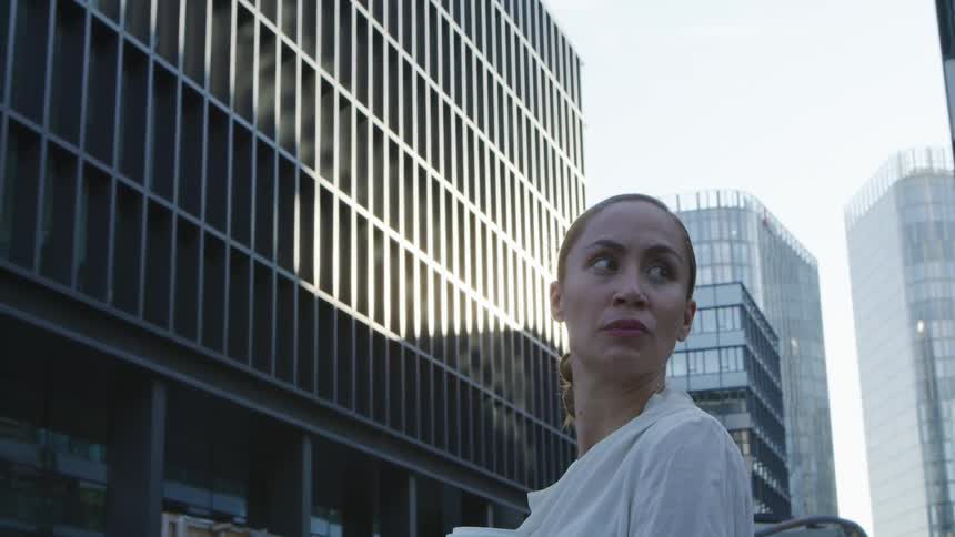 A woman gazes around at her surroundings while standing outdoors in a metropolis during the day