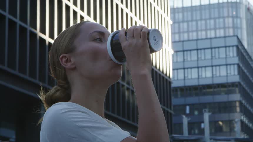 Woman stands near skyscrapers drinking from a portable cup of coffee