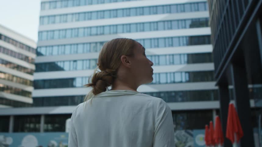 A woman examines the surrounding skyscrapers as she walks through a metropolis during the day
