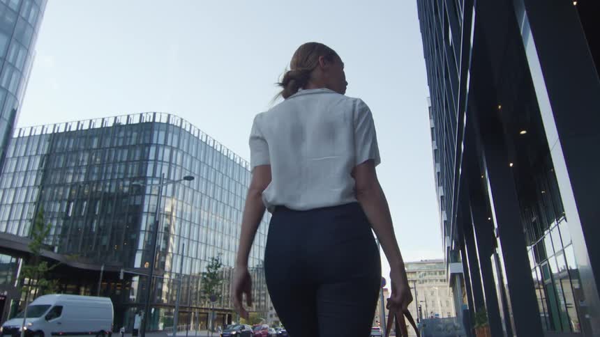 Blonde businesswoman with a white blouse carries a handbag walks on the pavement