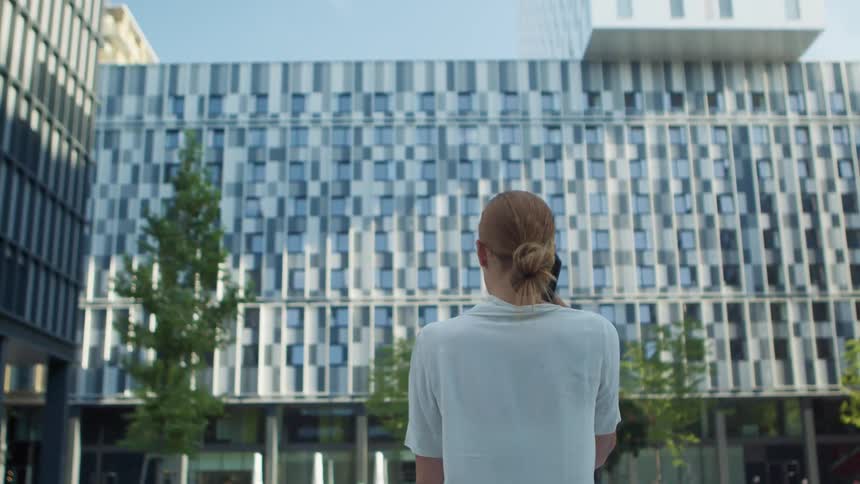 Blonde businesswoman with a white blouse talks on the smartphone in front of office buildings