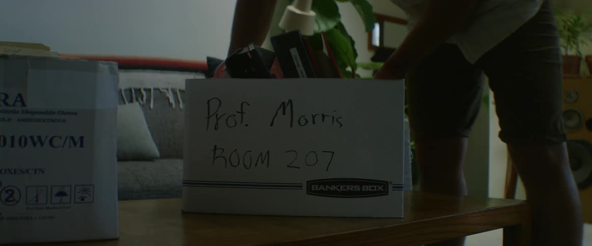 A man sets a moving box filled with binders on a coffee table in his house