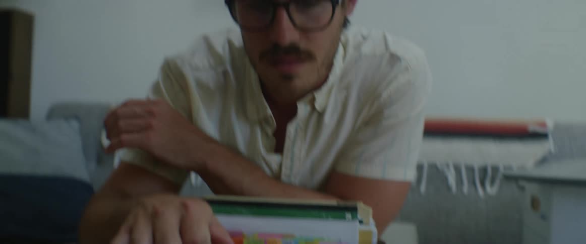 A man with glasses sitting on a couch and looking at a box full of books
