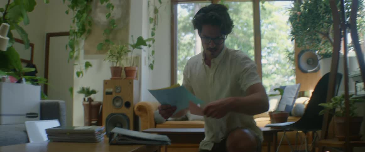 A man picks papers up off the floor at home and puts them in a binder