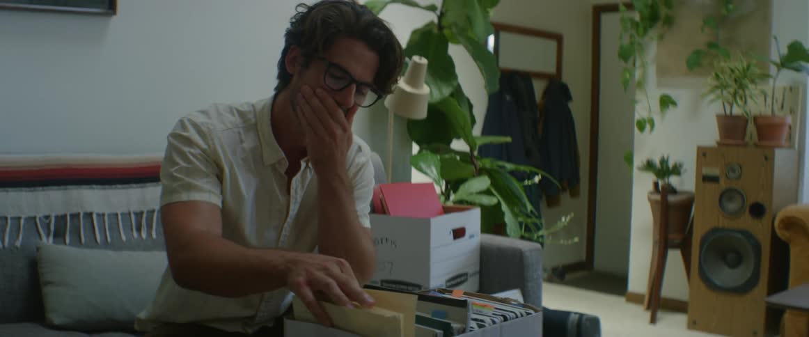 A man sits on his couch looking through a box of files