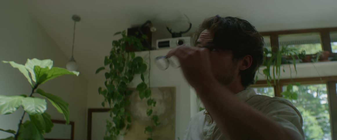 A man looks around a room assessing rubbing his face and removing his glasses