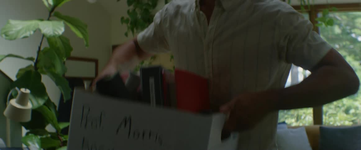 Man bringing a box full of books and folders into a living room