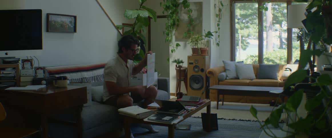 A man participating in a video chat on his laptop in his living room holds a white board in front of his laptop camera
