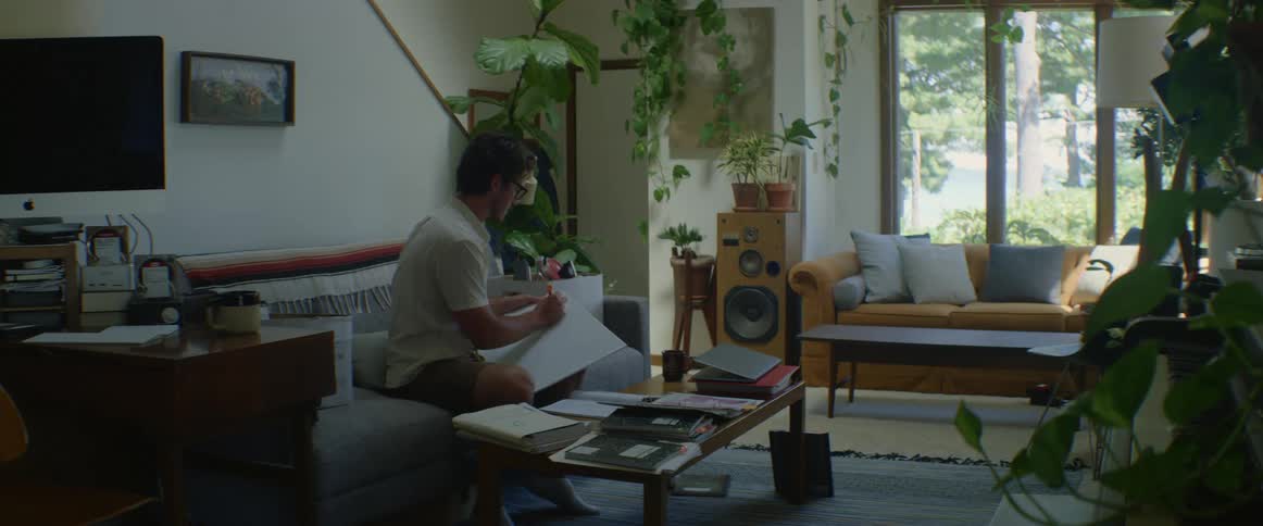 A man sits on a couch and writes on a large notepad