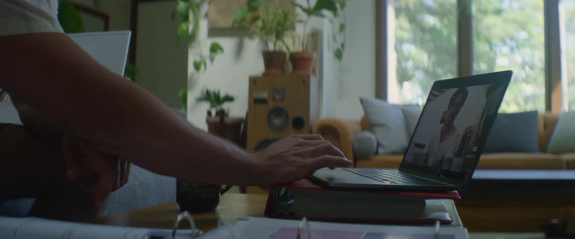 A man sits in front of a laptop and adjusts the screen for a video call