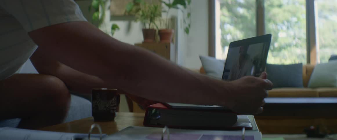 A man sits on a couch will placing a laptop and opening the lid in a living room during the day