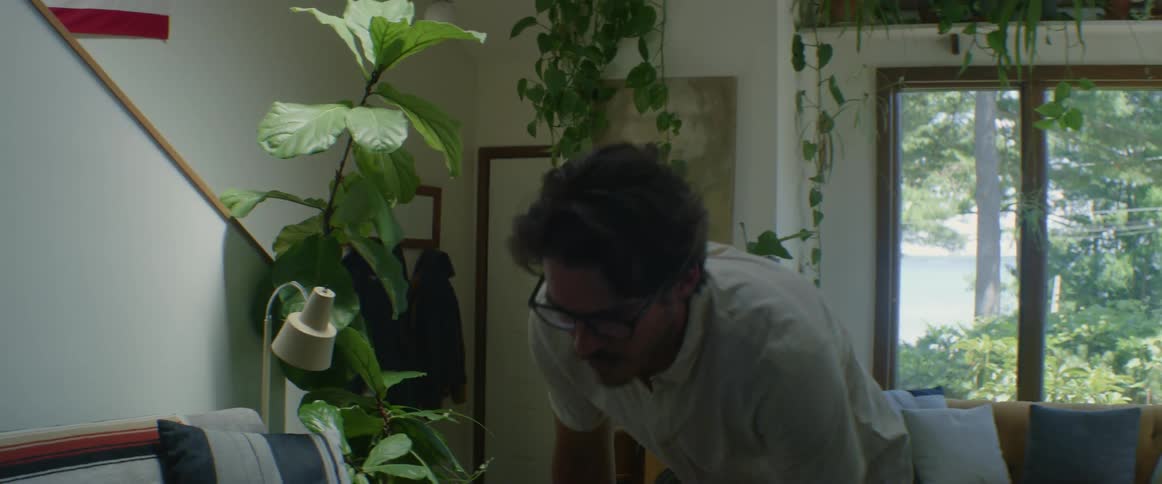 Man with glasses and a white shirt carrying a box enters the home