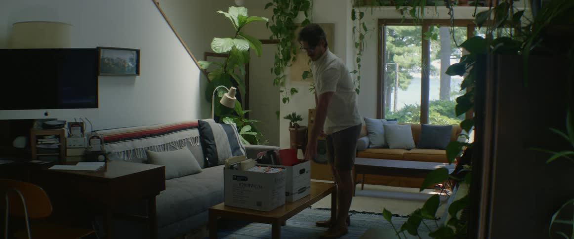 A man carries a box into his home and places it on a coffee table